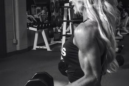 Side profile of Linda sitting on a bench, holding up 10 pound dumbbells